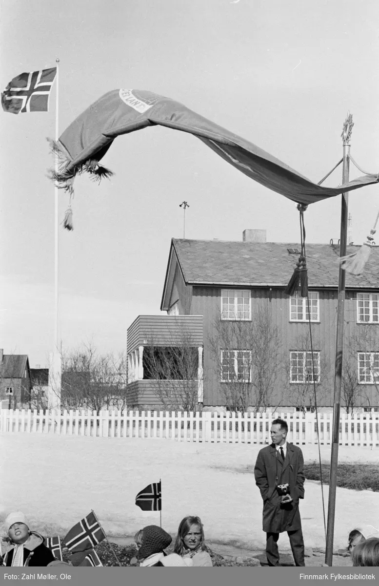 Vadsø 17.5.1969. Fotoserie av Vadsø-fotografen Ole Zahl-Mölö.  Vinden har fått godt tak i skolefanen. Skolebarn med flagg kan skimtes nederst i bildet.