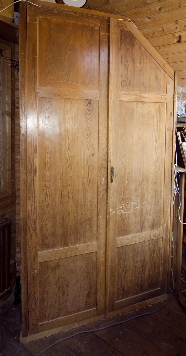 Väggskåp av trä för förvaring av kontorsmaterial m.m. Skåpet är uppbyggt på plats med sidoväggar, överdel och två dörrar. Baksidan utgörs av väggen på kontoret och trappan till övervåningen. Dörrarna är tillverkade med ram och fyllning. För låsets nyckelhål på den ena dörren finns mässingsbeslag. Skåpets överdel är vinklad för trappan till övervåningen på snickerifabriken. Skåpet är flyttat från Dahlgrens Snickeri i Nacka.

Funktion: Förvaring av kontorsmaterial