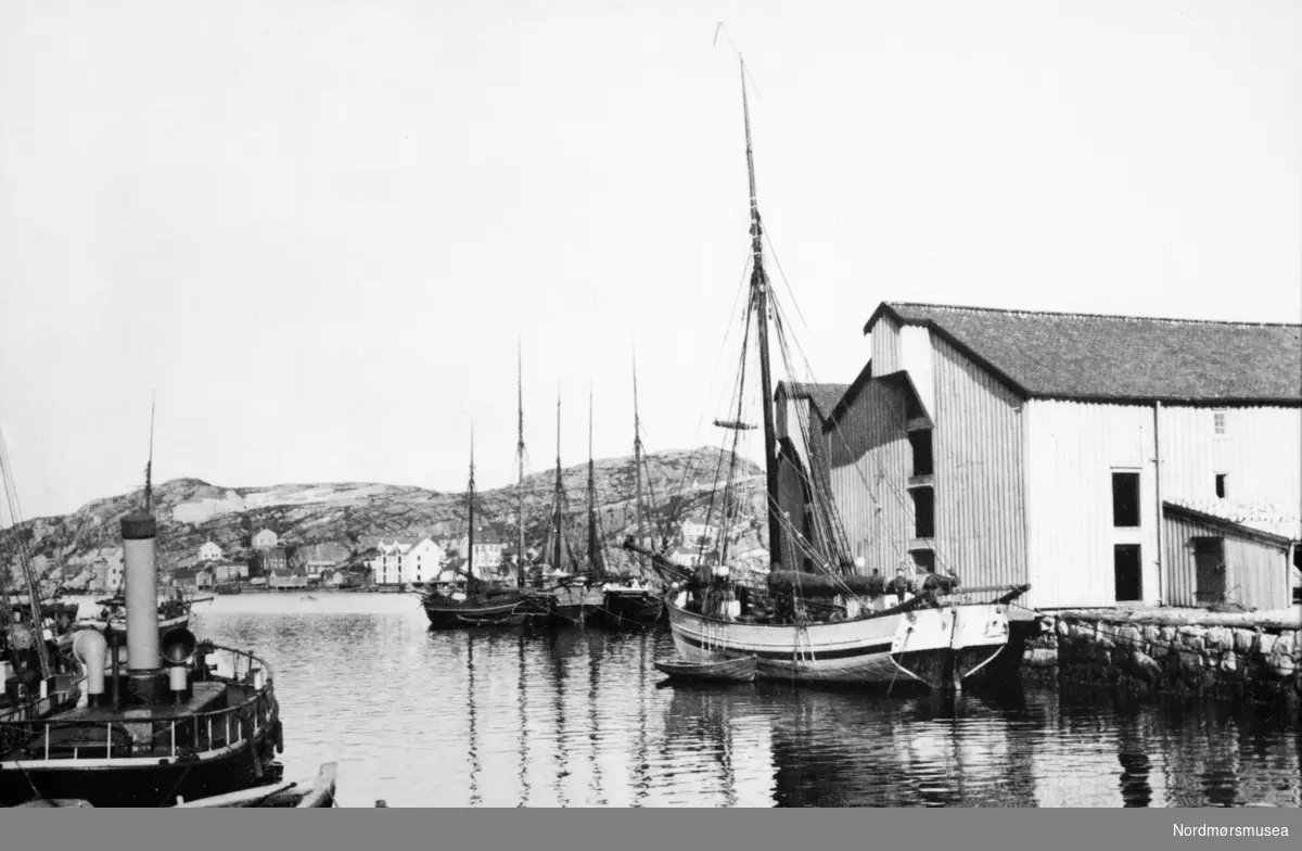 I forgrunnen til venstre er sannsynligvis brannsprøyta "Slukk", alle andre fartøy ser ut til å være jakter. brygger,  pakkhus i Kristiansund med en del fartøy liggende i nærheten. Datering er usikkert, men trolig rundt 1910-1920. Fra Nordmøre museums fotosamlinger.
