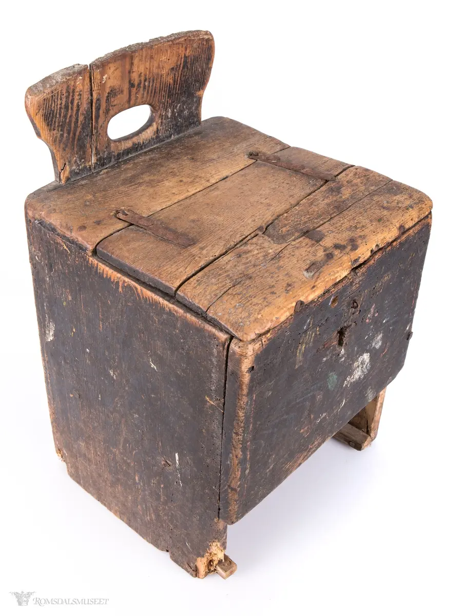 Trestol med kasse under setet. Ryggstøtten har en oval gjennomskjæring. På frontsiden er det et et nøkkelhull og en låsekork. Malte sidevegger.