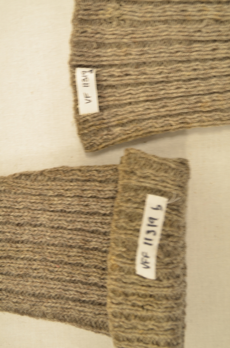 Lange strømper (a+b), strikket i koksgrått ullgarn. Ribbestrikka legg, 2 rette og 2 vrange. Stoppet under på hæl og tå med hvitt og grått garn