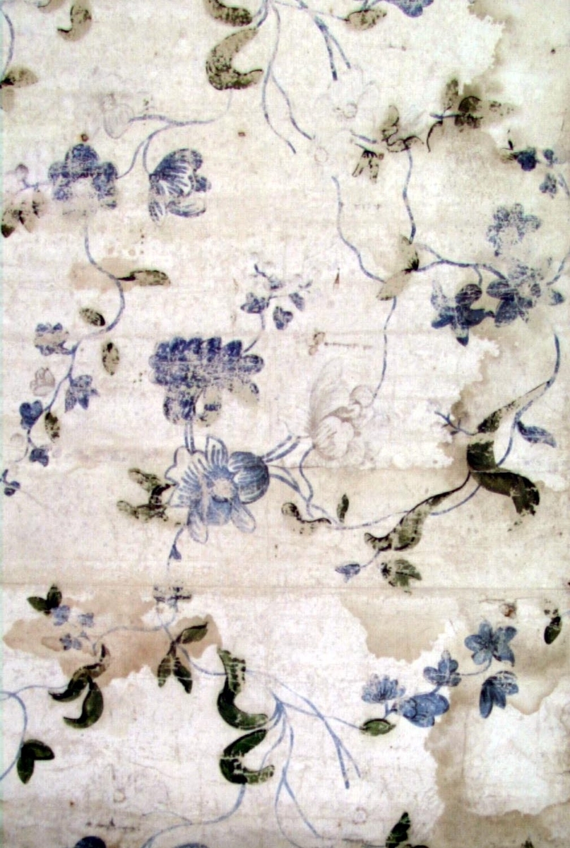 Ett stort vertikalt mönster med lätta blomsterrankor på en bakgrund bestående av sammanklistrade ark av lumppapper. Tryck i ljusblått, olivgrönt och något svart på en vit limfärgsbotten. Fransk rokokotyp.