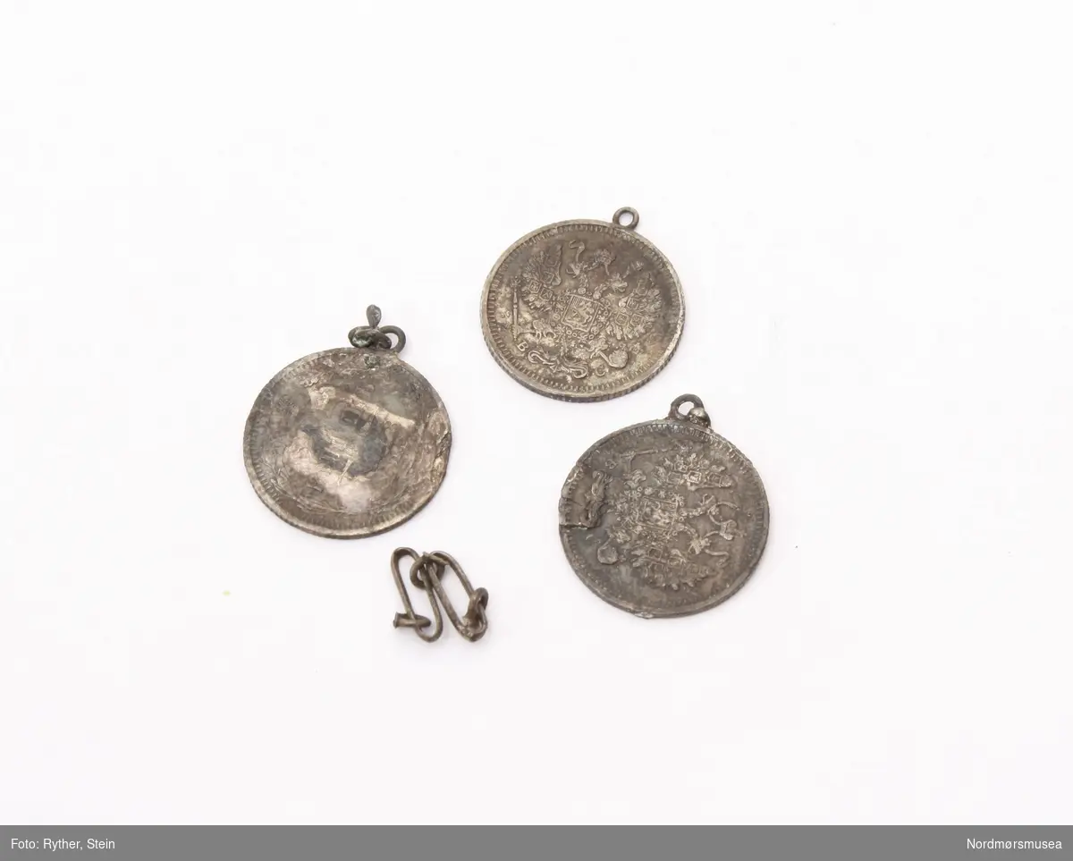 Forskjellig håndarbeid samlet i en eske som består av russiske mynter, omgjort til redskap og smykker. Esken består av 6 små mynter, 3 små mynter med anheng, 4 større mynter banket til en skålform, en skjei laget av en større mynt fra 1841 med skaft fra en opprinnelig skjei. Og en stift og to stenger i jern.

Alle myntene er russiske, og alle myntene er i metall.