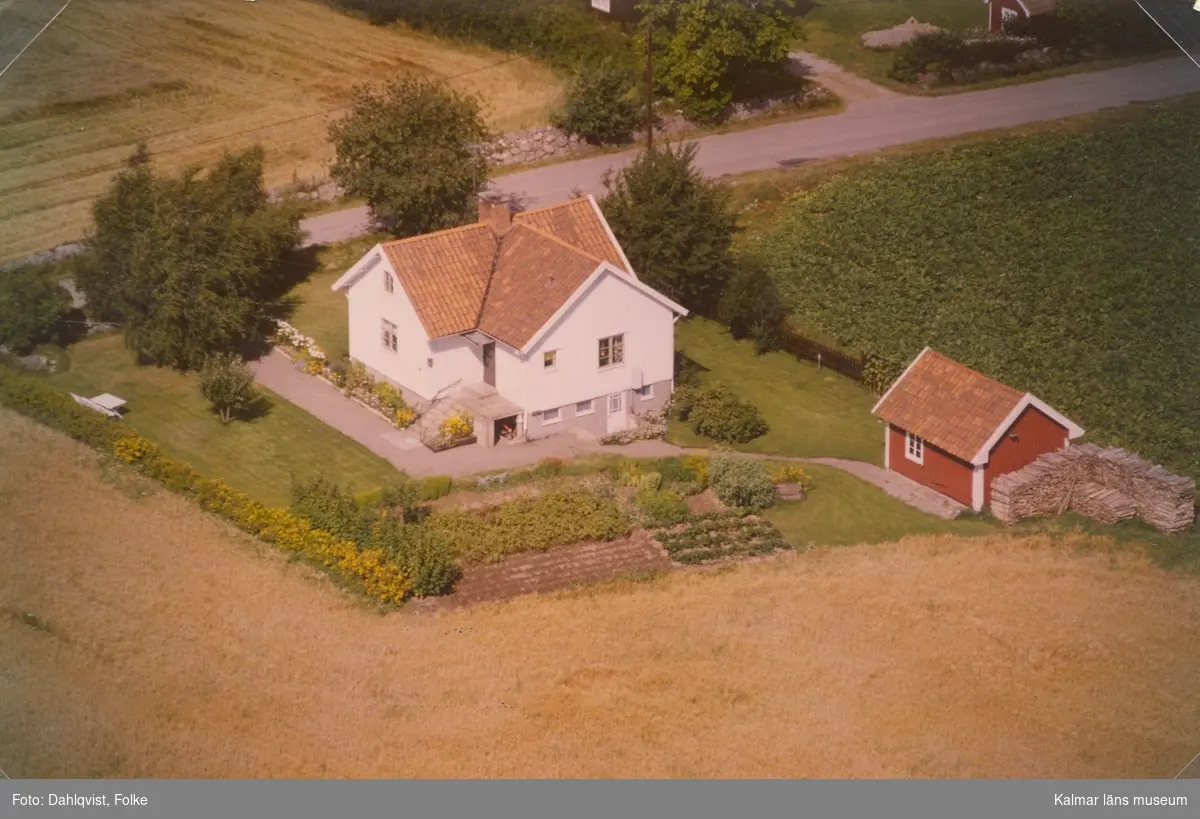 Bostadshus och sidobyggnad vid åkermarker i Arby socken.