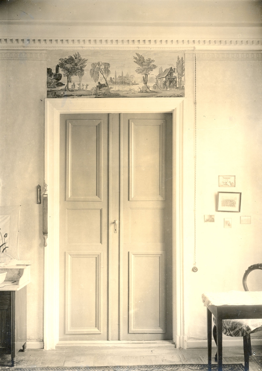 Övervåningen, rum sex. Dörröverstycken, två stycken tryckta mångfärgade på papper, fantasilandskap. Flat grå Kakelugn. Överstycket av Arthur & Robert 1781-1811,