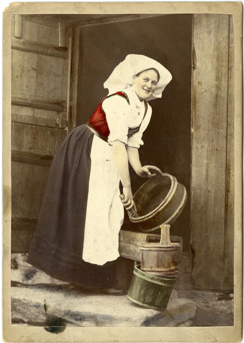 Kolorert fotografi av kvinne med drakt i døråpning med tre tiner. Hardanger.
