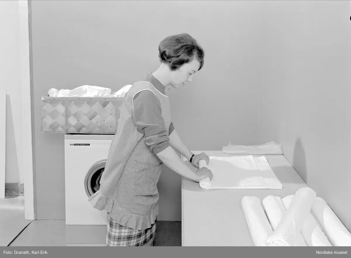 Tvättstuga. Kvinna förbereder lakan för mangling