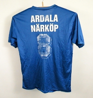 V- ringad, kortärmad tröja i ljusblått och mellanblått. På framsidan Ardala Go IF:s märke och på ryggen siffran 8 samt texten "Ardala Närköp". Se även 105569- 105612 samt bilaga till 105569.