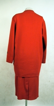 Röd maskinstickad kofta av ullgarn med tillhörande kjol ( 106259:2).
 Knappar av mässing med firmamärket "Busnel".
Har tidigare tillhört dottern Elisabeth (givaren)