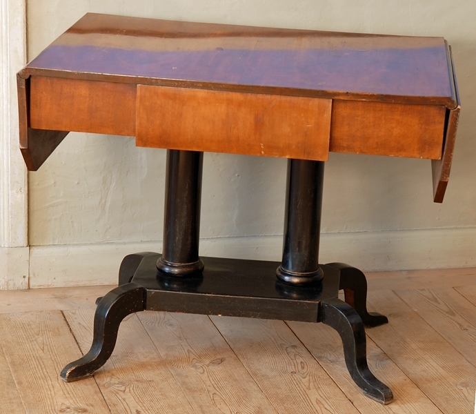 Rektangulärt bord med utdragslåda. Bordskivan och lådan är fanerad i mahogny. På båda sidorna skivan finns en liten klaff, uppfällbar genom gångjärn på undersidan. Klaffarna är 24 cm breda och har avrundade hörn. Skivan uppbäres av 2 svarvade kolonner med bas på en rektangulär platta 5 cm tjock. Vid plattans hörn sitter 4 st S-svängda ben. Hela underredet till bordet är svartpolerat trä.