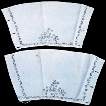 Ett par manschetter av vitt dubbelt bomullstyg. Broderad bladslinga i svart på tre sidor och i mitten ett blommönster. Vit kulknapp i en kortsida och tre knapphål i den andra.

Märkt "342"

Neg.nr: 1989-02