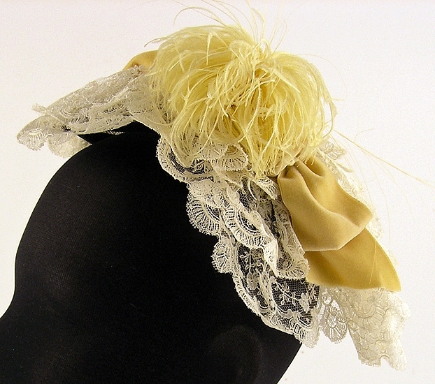 Hårklädsel av vit tyllspets, gula sammetsband och fjäder.

Neg nr 1985-09