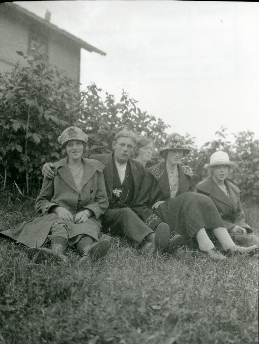 4 kvinner og en mann sitter på grasbakken foran et hus.