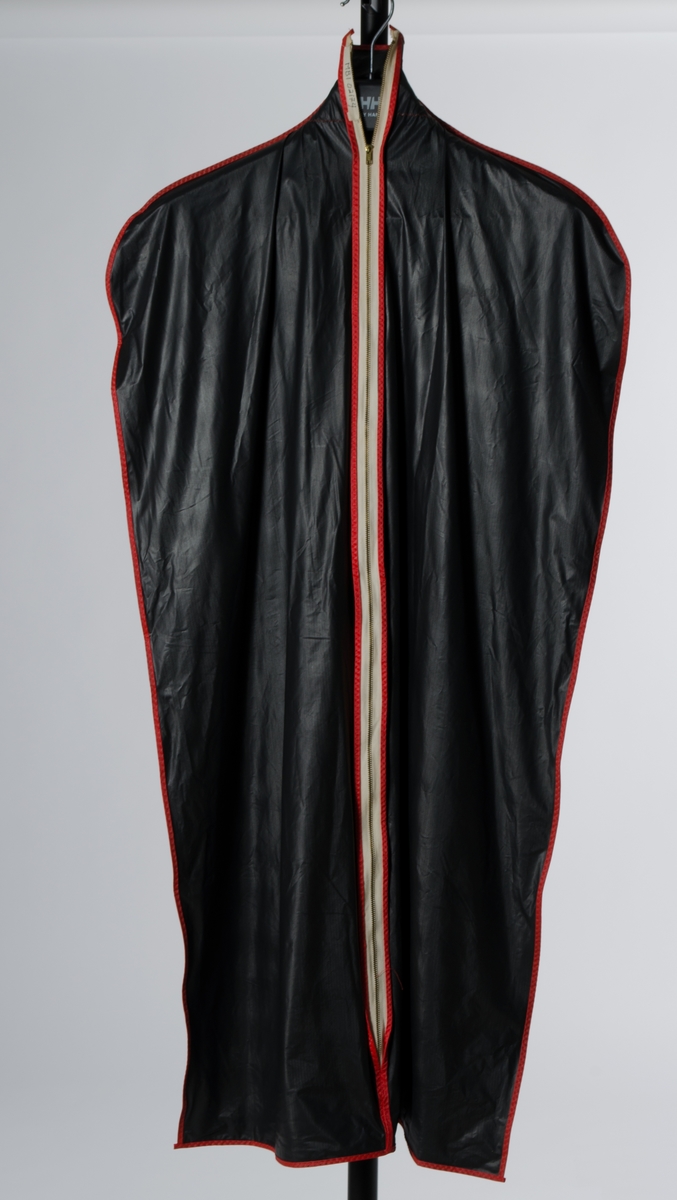 Flaskeformet garderobepose i svart helox, Hvit glidelås med røde kantebånd i plast påsydd med zig zag sting. Åpning øverste til å tre inn kleshenger.