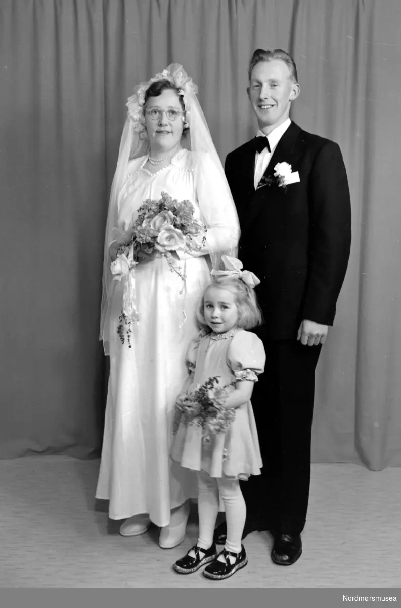 Foto av et brudepar, trolig med datter. Familien er sannsynligvis fra Tingvoll kommune i Møre og Romsdal. Datering er omkring 1950-1960. Fra Nordmøre museums fotosamlinger, Halås-arkivet.
