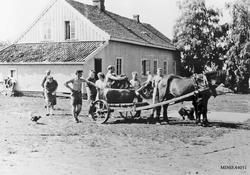 Hest, vogn, personer, bolighus.