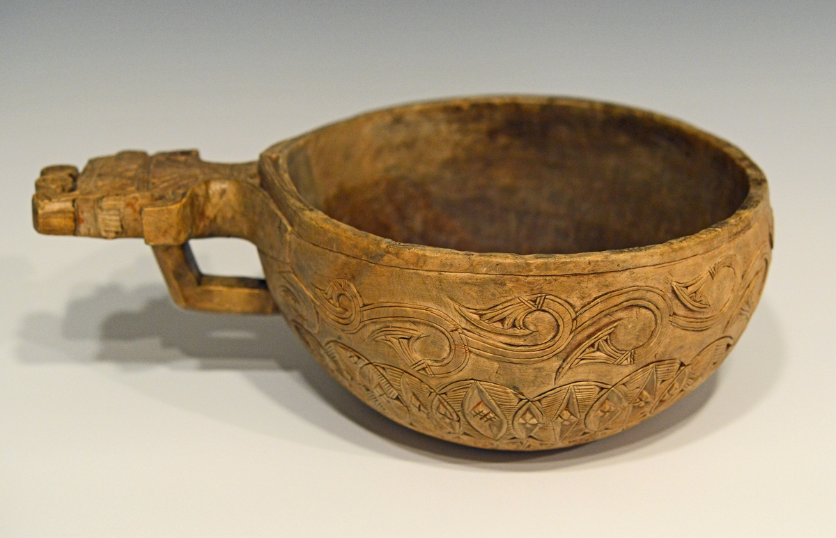 Oval øløse i tre med bredt skaft. Øløsen er dekorert med treutskjæringer i to border på korpus , samt utskjæringer på skaftet. Skaftet mangler en del av dekoren. Det er spor etter tidligere rødmaling.