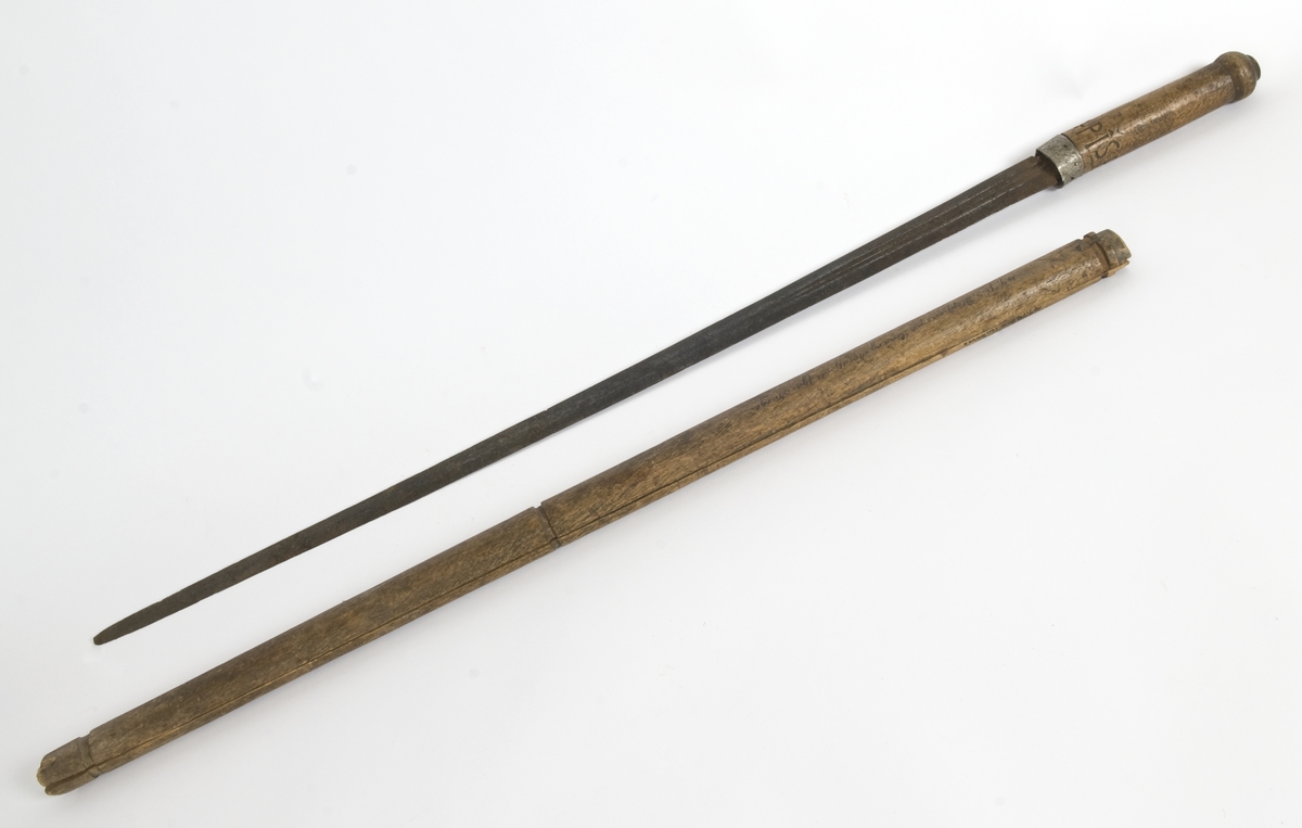Tregrep med hvitt metall ring nederst. Knappen er formet i treverk..Grepet har innskåret intialer PISH 1824.
Rett tveegget klinge med elipseformet tverrsnitt. To midtstillt smale blodrender.Dekor for enden av blodrendene på begge sider.
