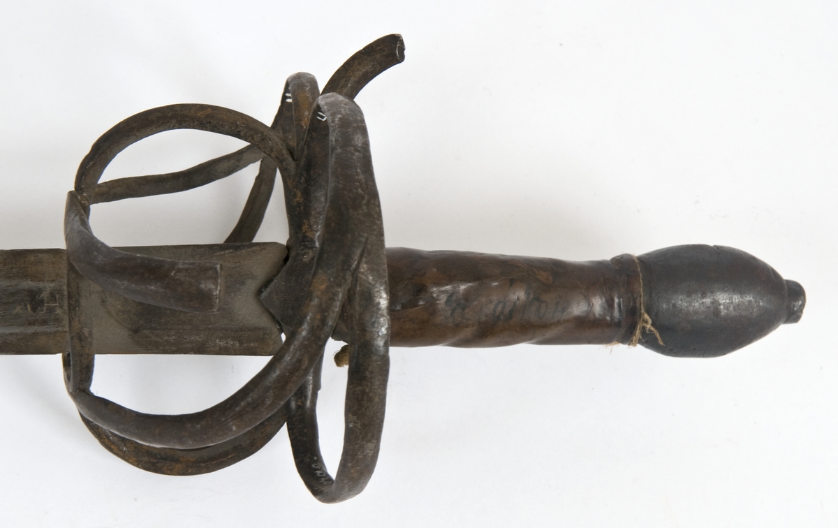 Avleng, plommeformet knapp med nitteknapp. Tregrep med lær bevikling. Asymmetrisk feste med flate bøyler. Fremre parerstang går over i håndbøylen. Sidering. 
Tvenegget, rett klinge med elipseformet tverrsnitt. og 1 kort midtstillt  blodrand på hver side.. Klingen er merket med  Passau-ulv på utsiden og smedmerke på innsiden.