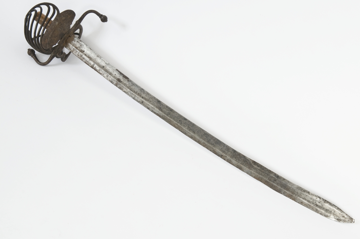 Knapp mangler. Tregrep. Asymmetrisk feste med runde bøyler. Fremre parerplate er nyreformet, og innsiden har tombøyle og klingebrekker. S-formede parerbøyler som ender i en kule.  
Enegget klinge med bred blodrand og ryggslipning mot spissen.  Gjeddenebb.  Smedmerke på innsiden.
Balg medfølger.  Trebalg trukket med 2 lag lær. Balgen er i dårlig stand.