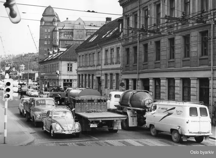 Trafikken i Rådhusgata, sett fra hjørnet ved Dronningens gate 8 B. Trafikklys. Havnelageret i bakgrunnen.