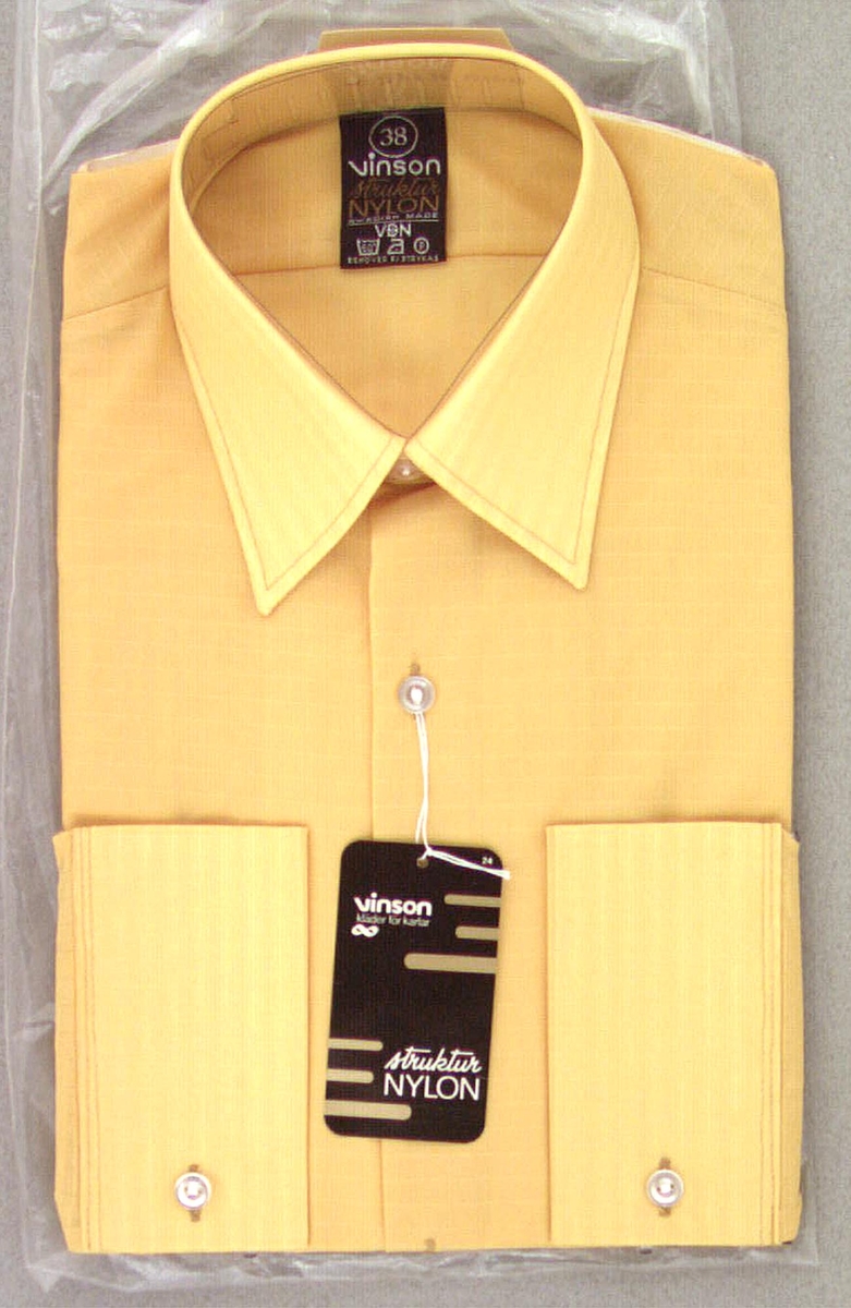 Gul nylonskjorta i originalförpackning av märket Vinson. Storlek 38. Ligger i plastpåse som också är i original. Svart märkeslapp i halsen med storlek och tvättanvisning. Måtten avser skjortan i vikt tillstånd.