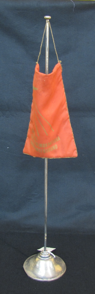 Bordsflagga av rött tyg med en bård av guldfärgad metalltråd runt tre kanter. På ena sidan visar 
flaggan i guldtryck en örn vilken flyger genom tre strålar. Nedanför bilden står ''SVERIGES 
SOCIALSEMOKRATISKA UNGDOMSFÖRBUND''. Örnen visar på ungdomsförbundets namn ''Unga
 örnar''. Flaggan mäter : H . 15,4 cm B. 23 2 cm.

Flaggan står på ett stativ av silverfärgad metall med rund fot. stativets mått: Diam  11,6 cm H. 63 cm.

21 459: a Flagga
21 459:b  Stativ
