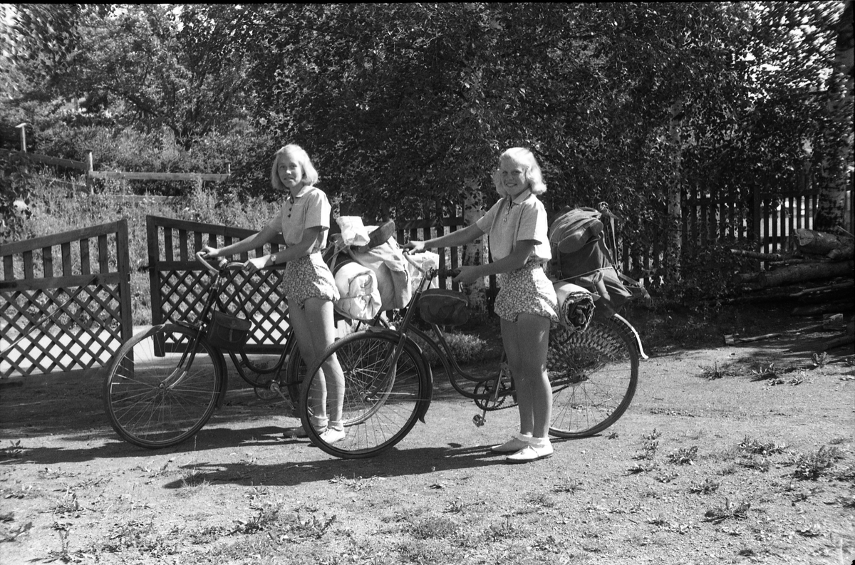 Sigrun Røisli og Astrid Kolstad klare for sykkeltur juli 1948. To bilder. På det første avbildet på gårdsplassen på Odberg, det andre på vegen like etter start.