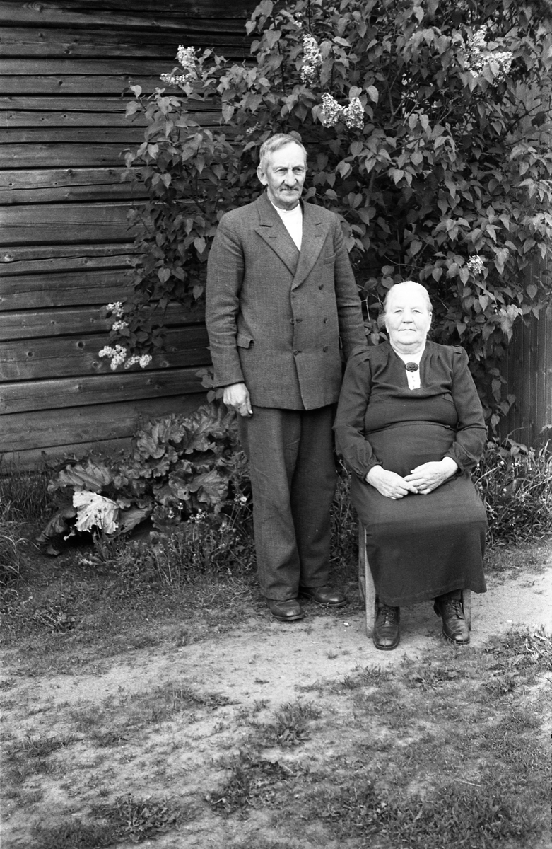 Helfigurs portrett av et eldre ektepar. Personene er Olaf Lauritzen Nygaard og kona Mina Halvorsen Nordengen, begge oppvokst og gift i Hurdal. Stedet er bruket Nygård i Haugstadgutua, Øverskreien, der de bodde.