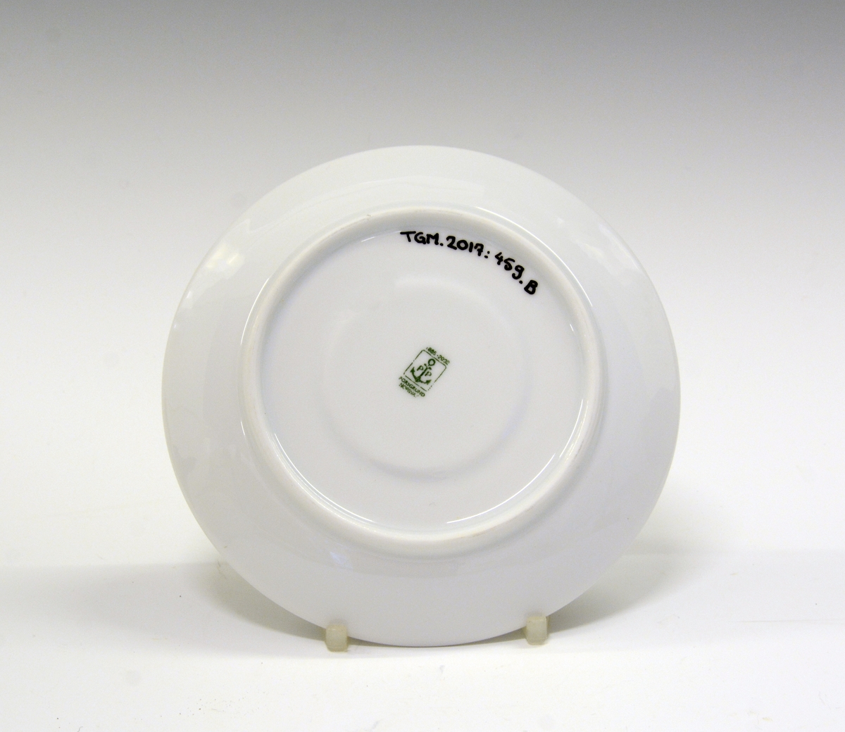 Kaffeskål av porselen. Hvit glasur. Dekorert med blå stripe ytterst på fanen og tre smale blå striper med noe grønt på innerst på fanen.
Modell: Roma