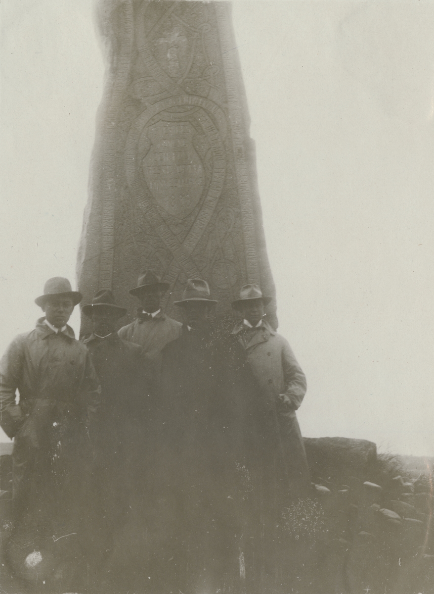 Grupp män samlade vid ett monument.
