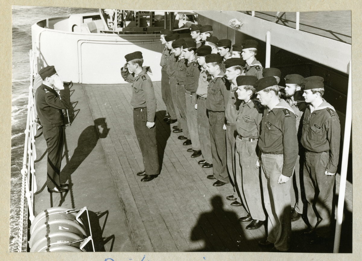 Bilden föreställer uniformsklädda besättningmän uppradade på däck ombord på minfartyget Älvsnabben. Aspiranterna i 1.kvarteret lämnas av till dess kadettunderofficer, flaggstyrman Oskar Linde.