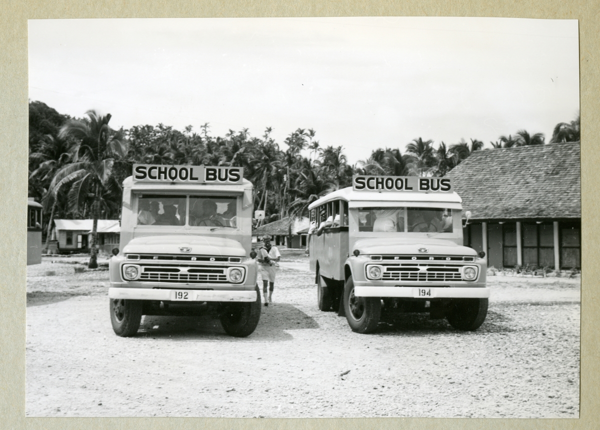 Bilden föreställer två skolbussar framifrån. I bakgrunden syns viss bebyggelse samt växtlighet med palmer. Bilden är tagen under minfartyget Älvsnabbens långresa 1966-1967.