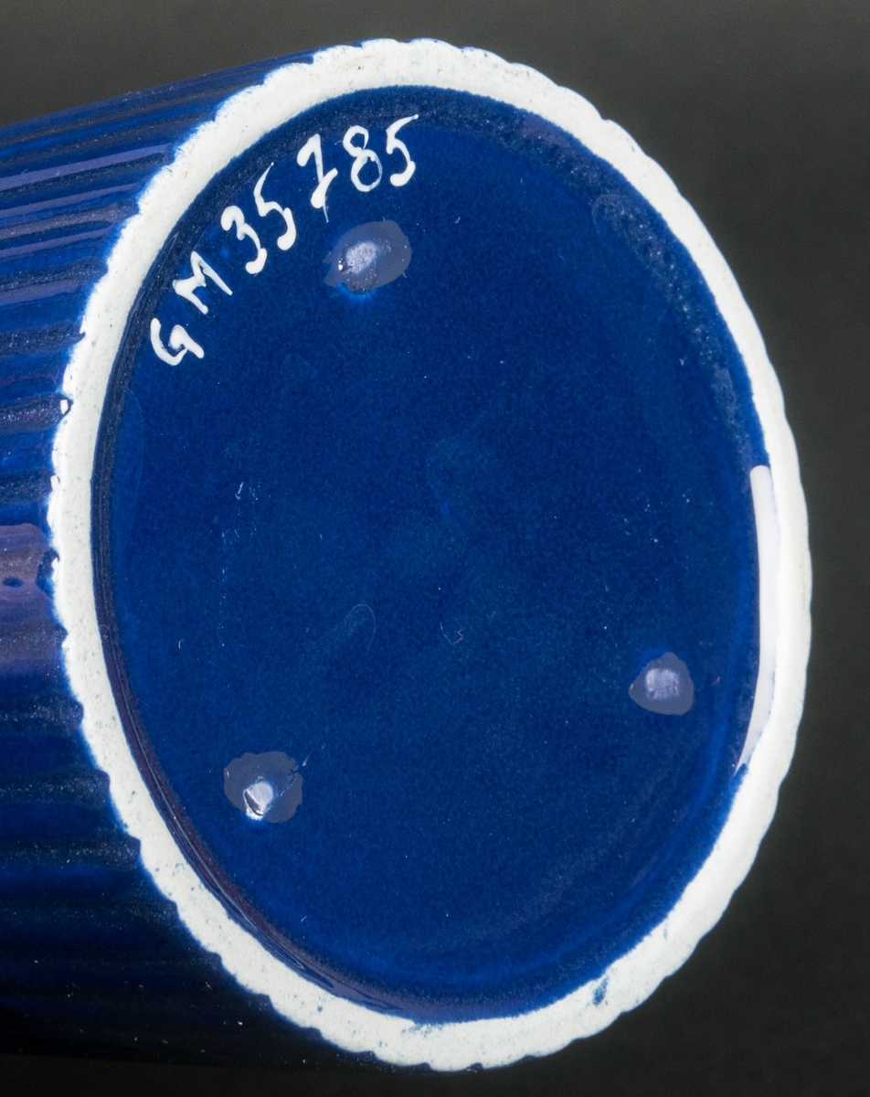 Kaffekanna med lock i cylinderform. Räfflad dekor och med stark blå färg. Ostämplad. Formgiven av Arthur Percy vid Gefle Porslinsfabrik, 1950-tal. 
Hör samman med gräddkannan 35786.