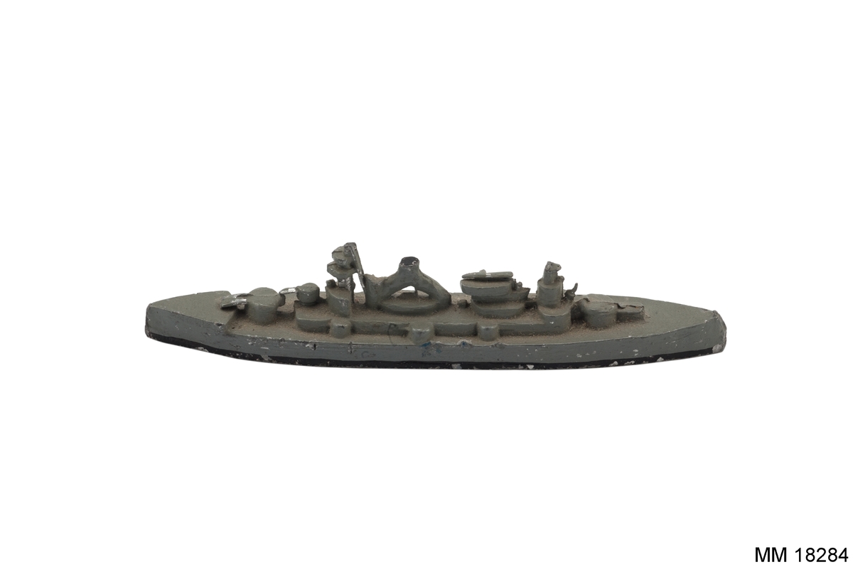 Fartygsmodell i form av pansarskeppet Gustav V gjuten av metall i ett stycke, målad i grått, svart längs vattenlinjen. Spetsig för och akter. Plan botten. Artilleripjäser i för och akter, torn.