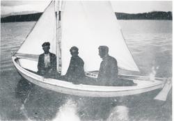 Tre menn i en robåt med segl.