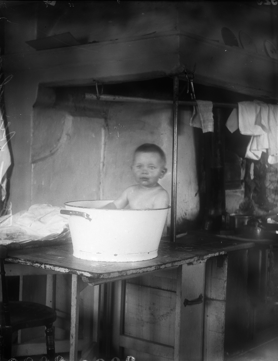 Tore Alinder badar i balja på bord i köket, Sävasta, Altuna socken, Uppland 1925