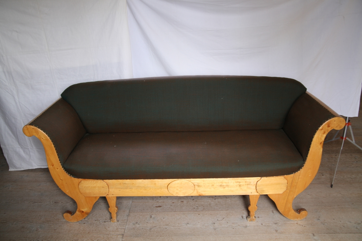 Sofaen har avrundet rygg og sidelener, fire par bein. Setet og ryggen er trukket med grått og brunt stoff.