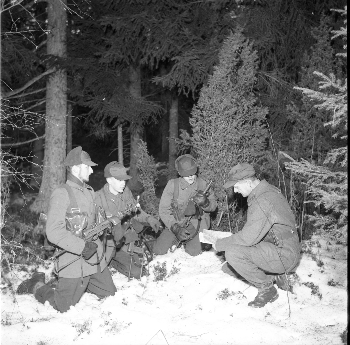 A6 håller övning i Haurida. Tre okända unga än med kpistar sitter på knä i snön och lyssnar till äldre officer som visar på en karta.