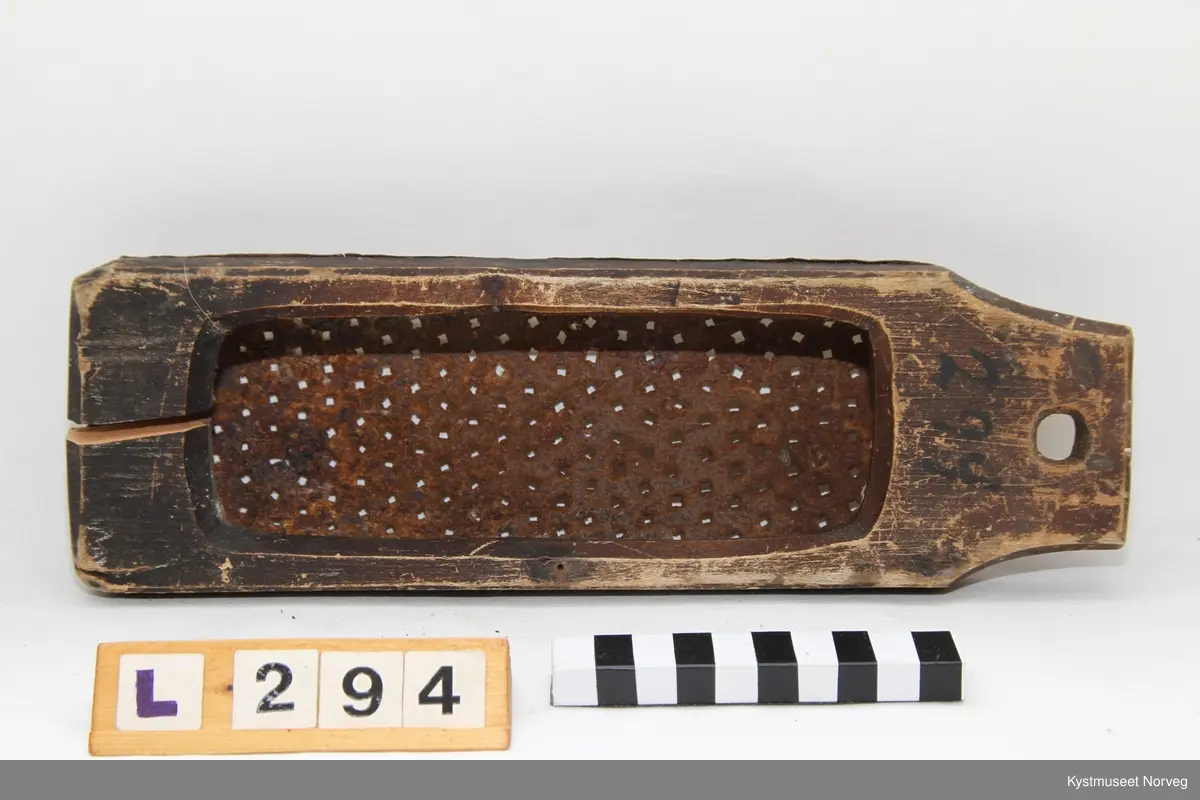 Potetrasp. Laget ved at et trestykke er tilskåret med opphengshull i ene enden, og stort hull inni som er tilpasset selve rivjernet. Rivjernet er utformet av et buet blikkstykke, der det er laget mange hull med spiker. Blikkstykket/rivjernet er spikret fast på trestykket.