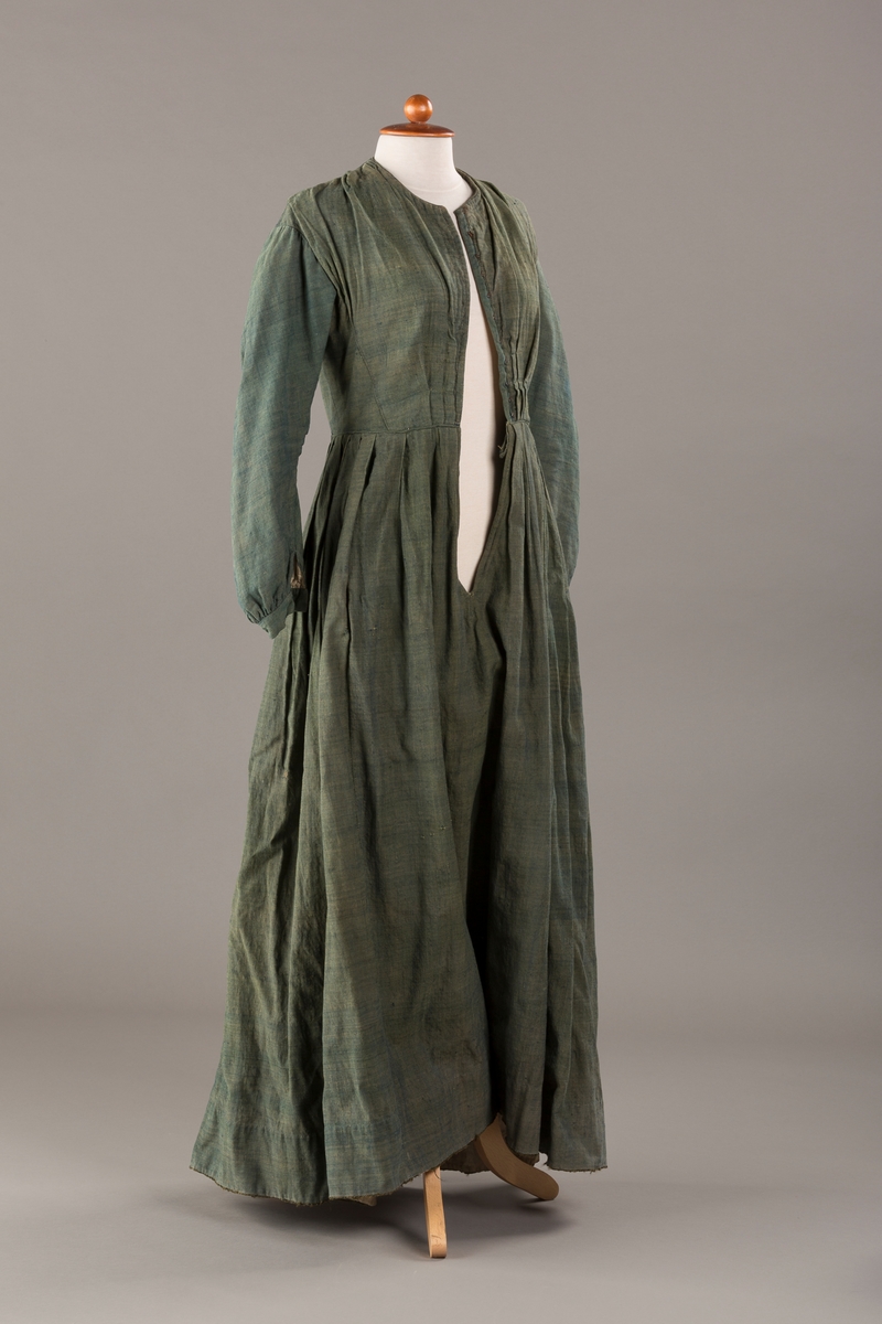 Form: Trangt liv med legg foran, skjørtet sydd med legg i livet.  God vidde i skjørtet, lange armer. Fem hekter i livet mangler.