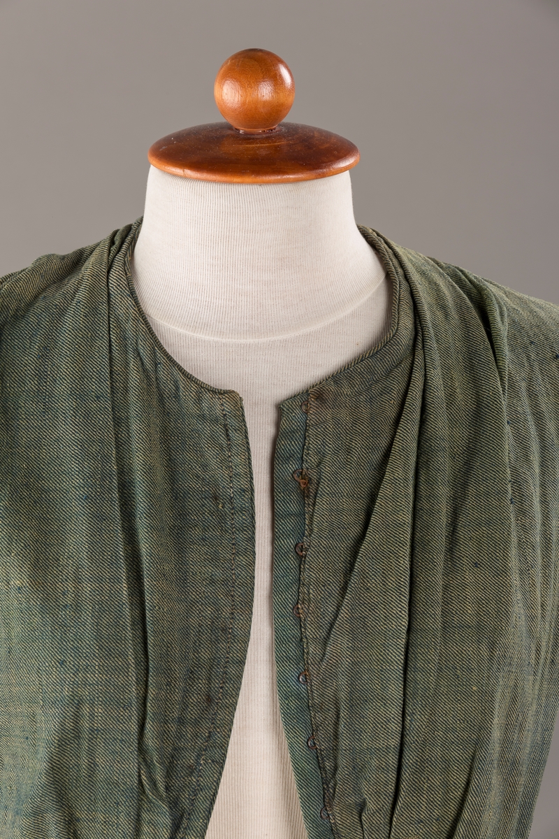 Form: Trangt liv med legg foran, skjørtet sydd med legg i livet.  God vidde i skjørtet, lange armer. Fem hekter i livet mangler.