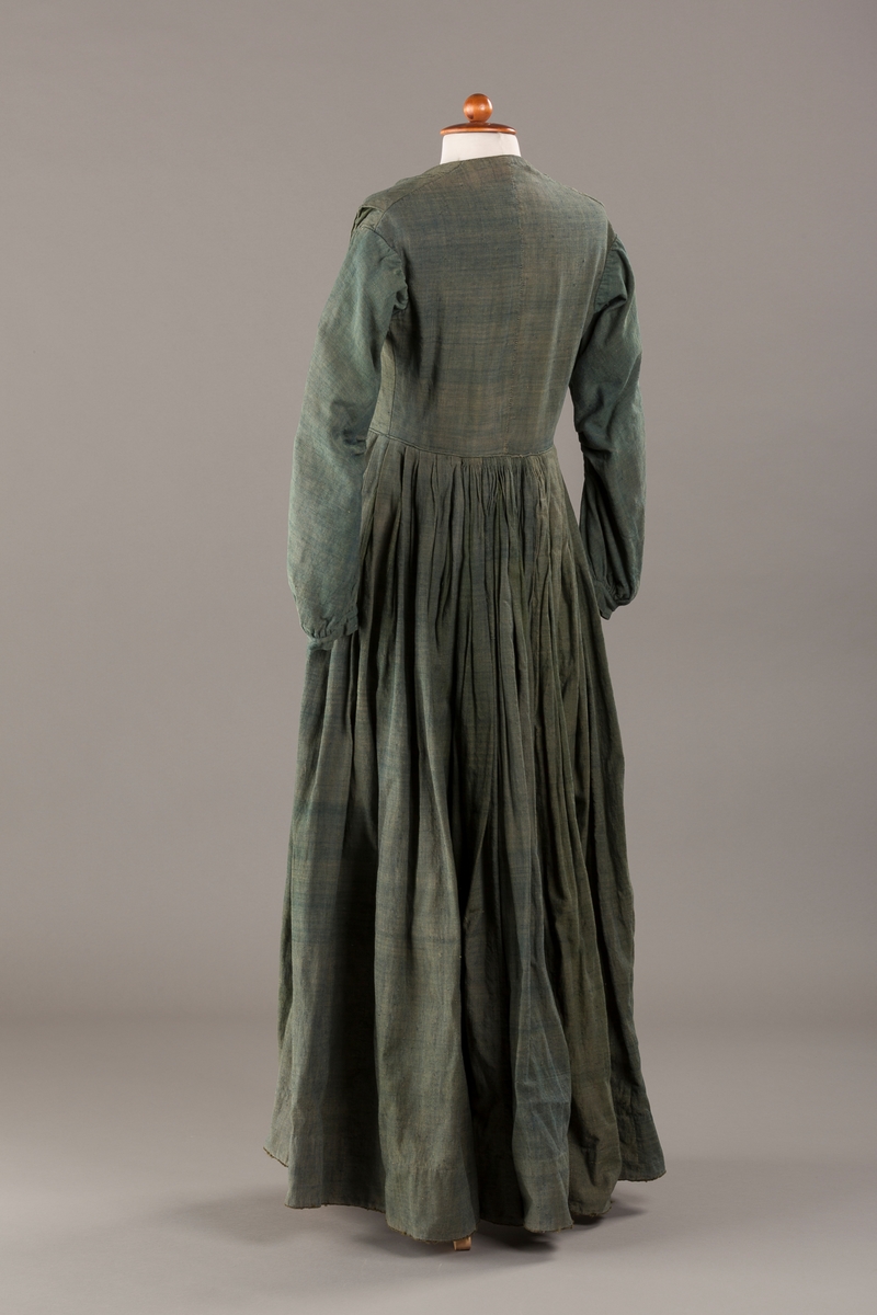 Form: Trangt liv med legg foran, skjørtet sydd med legg i livet.  God vidde i skjørtet, lange armer. Fem hekter i livet mangler.