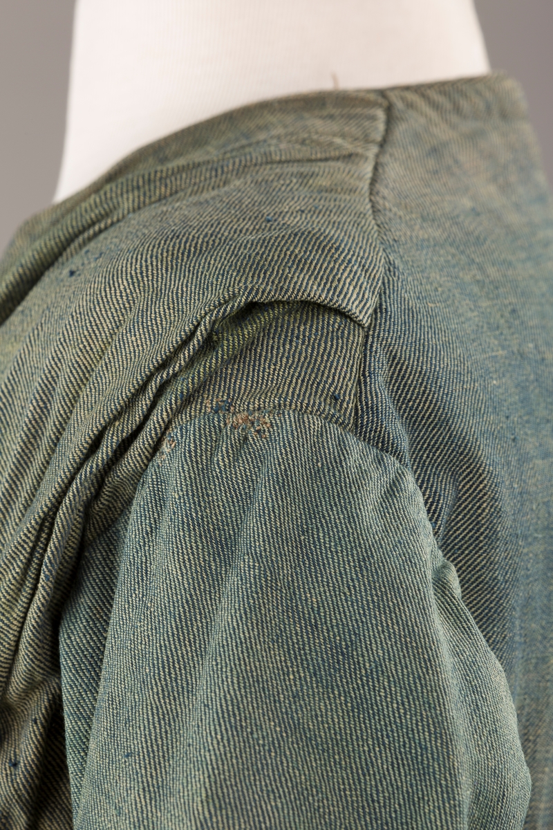 Form: Trangt liv med legg foran, skjørtet sydd med legg i livet.  God vidde i skjørtet, lange armer. Fem hekter i livet mangler.