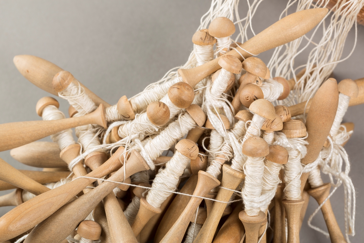 Form: Sylinderformet "pute" hvor stivt pappstykke rundt puta viser mønsteret. 
Kniplingsstykke under arbeid påspent med knappenåler
Pinner medkniplingstråd