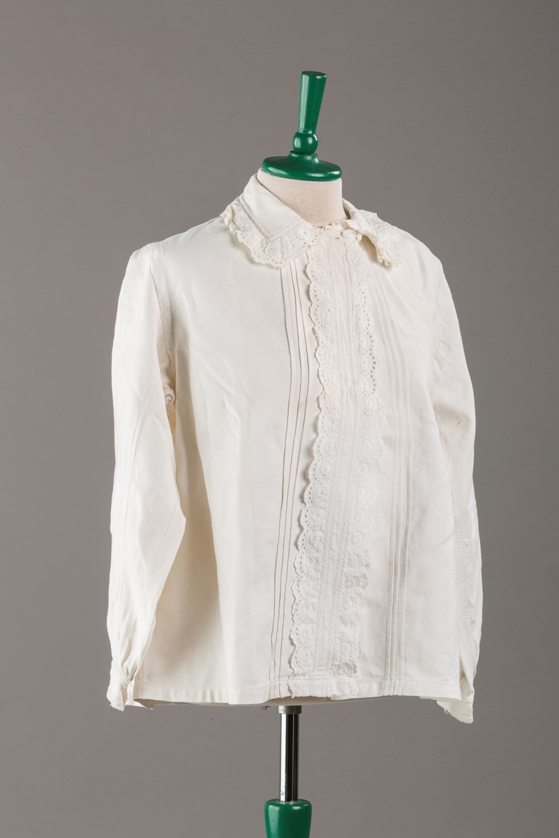 Form: Hoftelang trøye, Lange ermer, krage. Kragen og åpningen foran er kantet med  maskinprodusert blonde. Tre biser på hver side av åpn. foran. Lukkes med to løse knapper.