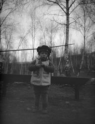 Liten gutt med matroslue står ute forran en benk.