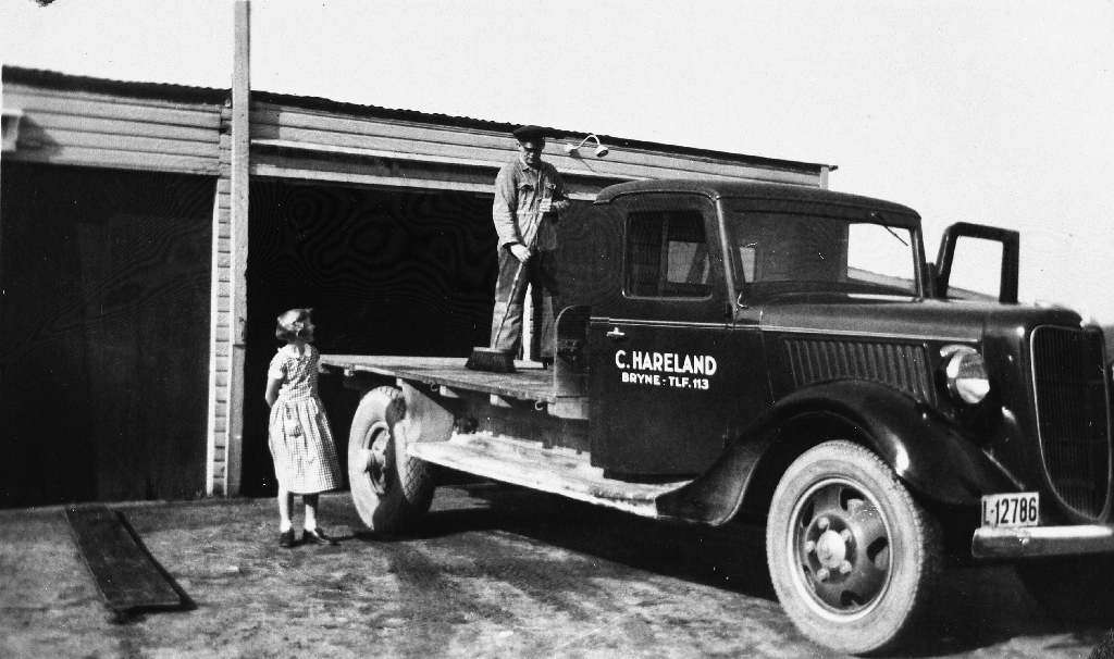 Ingrid Hareland g. Borge (11.7,1926 - )  ser på mens faren Charles Hareland (31.10.1896 - 15.5.1979) kostar av lasteplanen etter eit transportoppdrag. Han dreiv transportforretning på Bryne. Bilen, ein Ford, må vera temmeleg ny her.