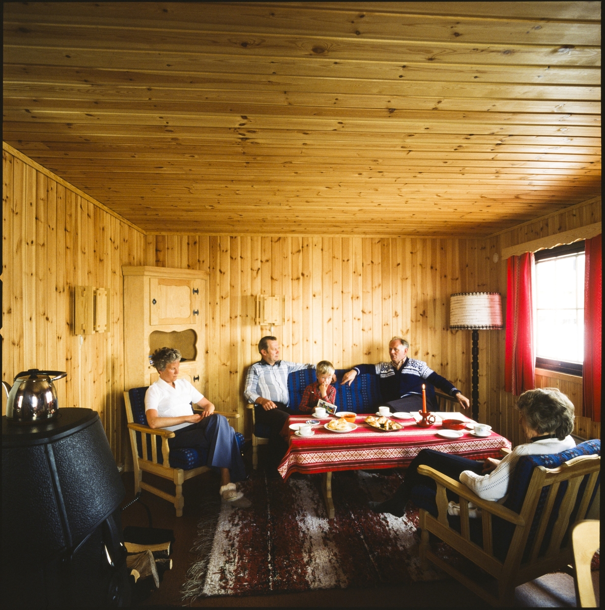 Fire voksne og et barn sitter ved et dekket kaffebord i en av Norsk Hydro sine hytter på Vågslid.