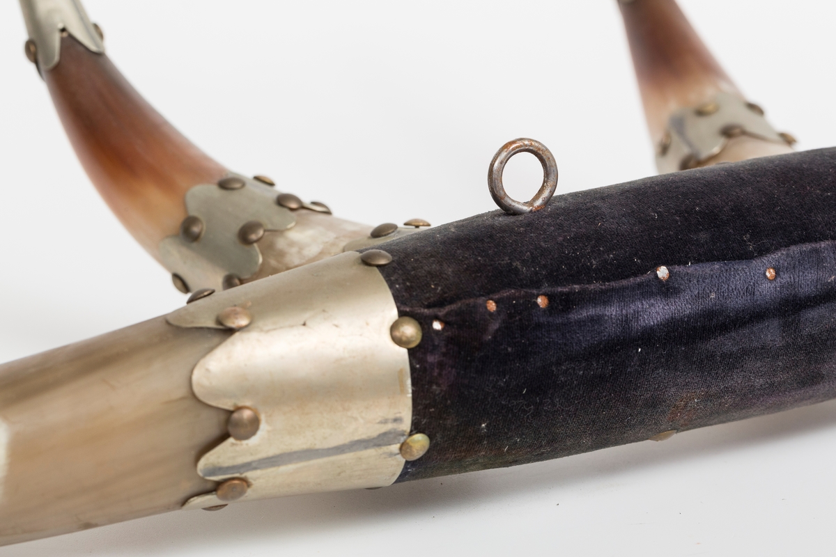 Knaggrekke antagelig håndlaget av kuhorn. 4 horn/kangger. Montert med "dekorative" beslag som er spikret og dekornaglet på hornene. Kledd med cordfløyelstoff på midtparti. To øyeskruer på toppen for feste til vegg.